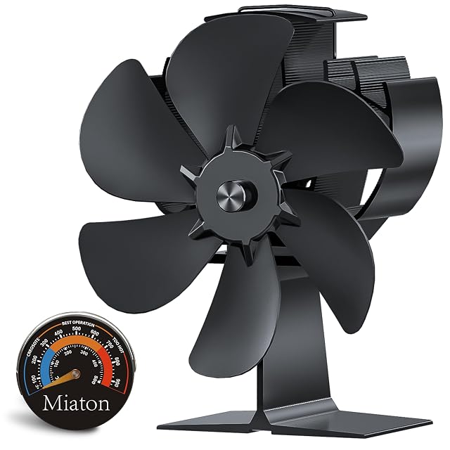 Ventilateur de poêle Miaton noir anodisé à six pales inclinées, à côté d’un thermomètre de poêle magnétique rond